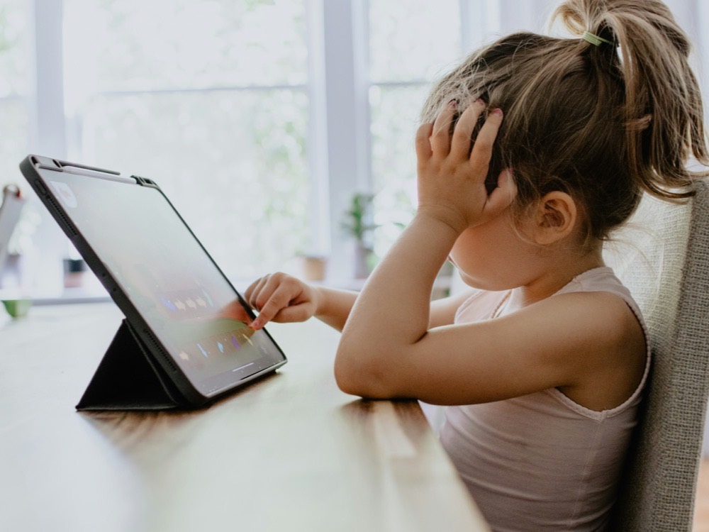 A young girl using a tablet at the kitchen table in bright daylight