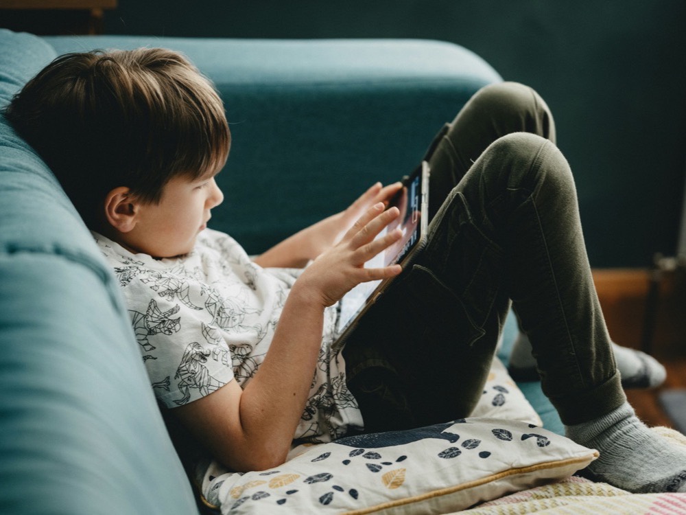 A boy relaxing on the couch with a tablet in soft window light