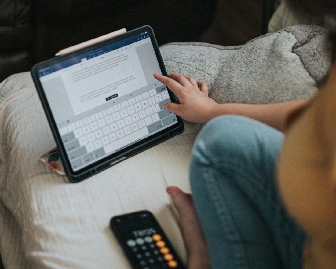 A parent reading on the couch with a tablet in a calm, lamp-lit room