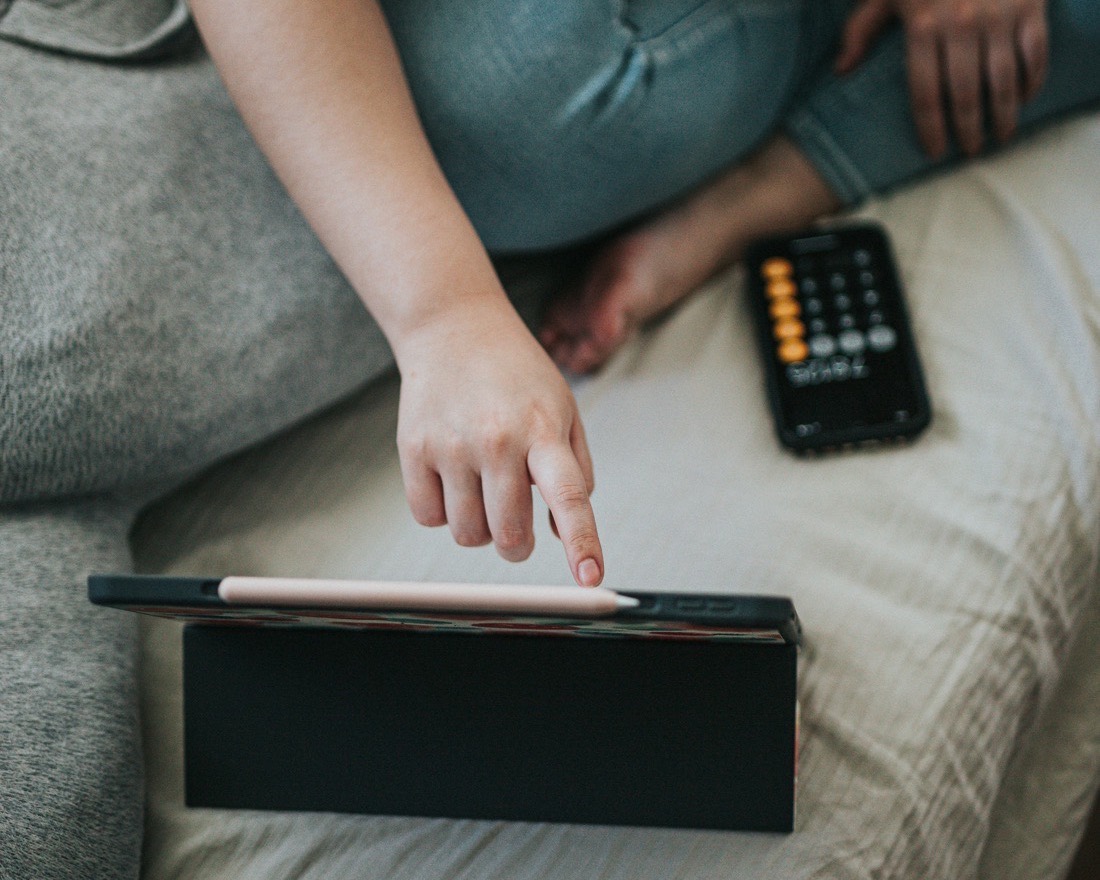 A hand reaching toward a tablet propped on a couch in soft daylight