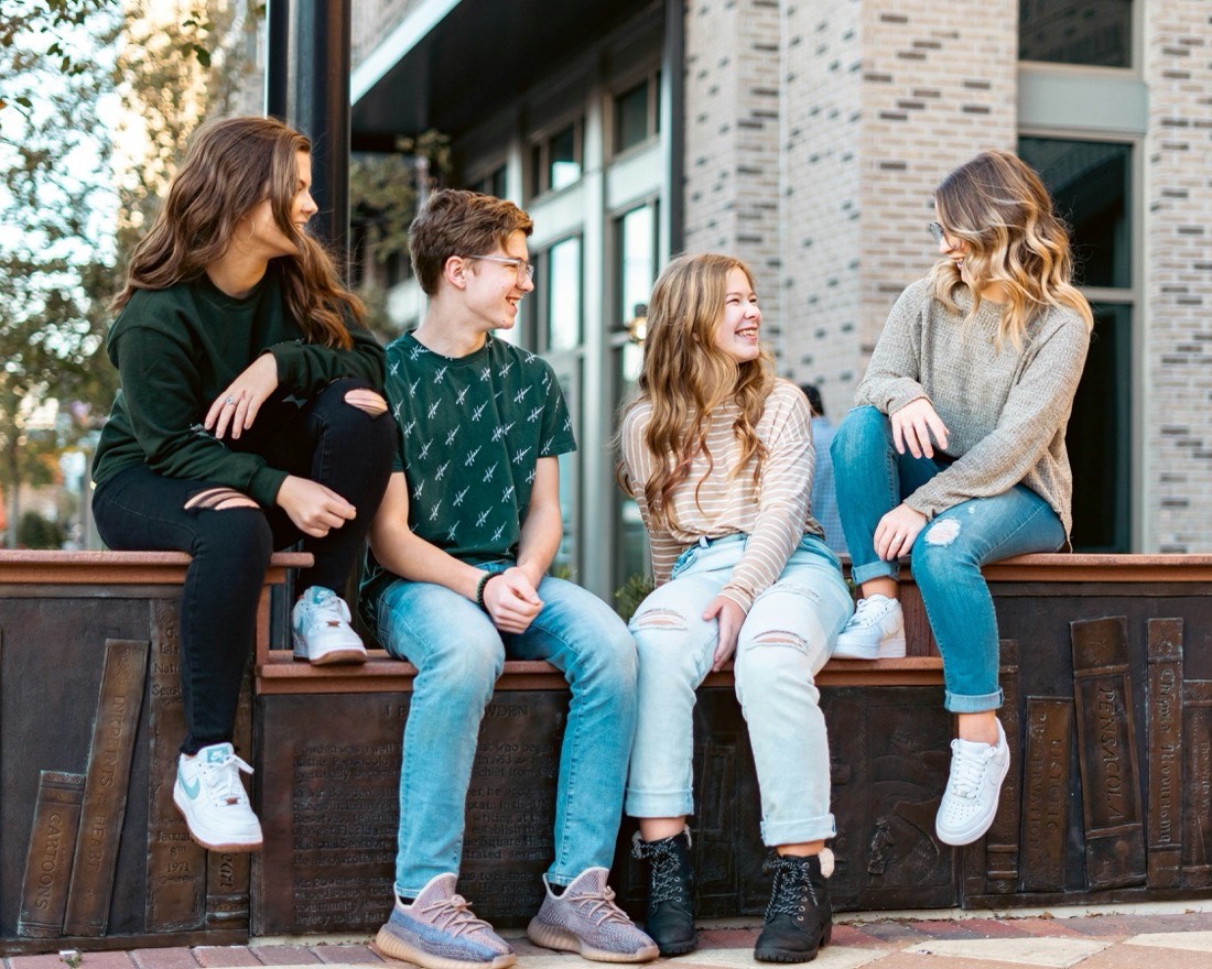 Four teenagers laughing together outside on a sunny afternoon